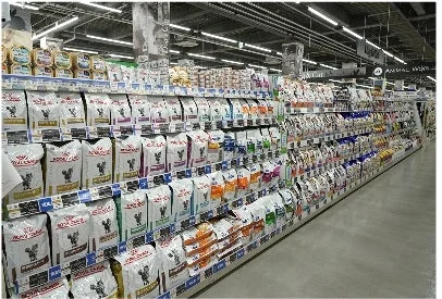 ペットショップの広々とした通路で、ロイヤルカナンなどの様々な種類のペットフードが棚にぎっしりと整然と陳列されています。多くの商品が並び、明るく整理された売り場の様子がうかがえます。