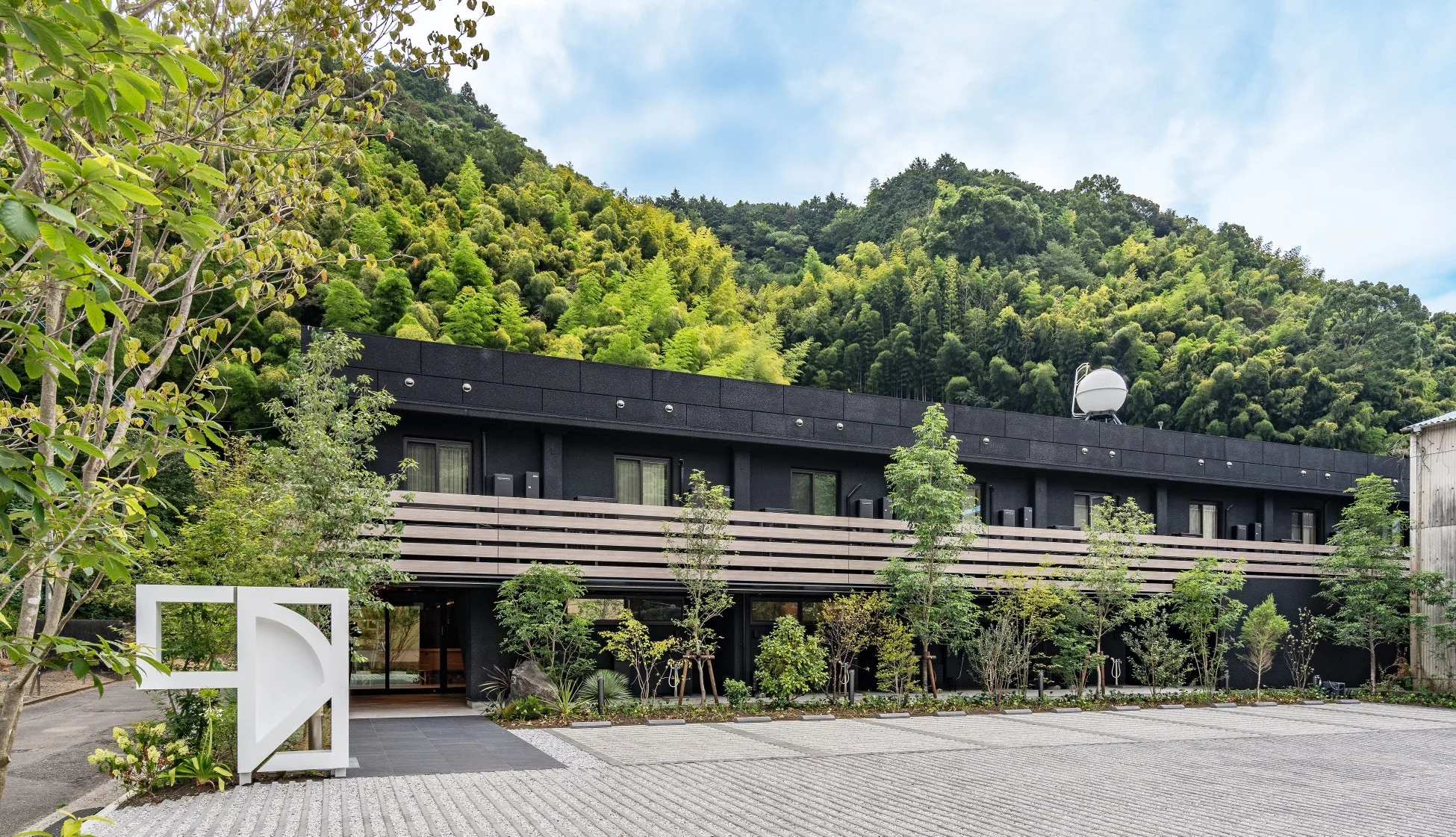 緑豊かな山を背景に建つ、モダンなデザインの黒い建物